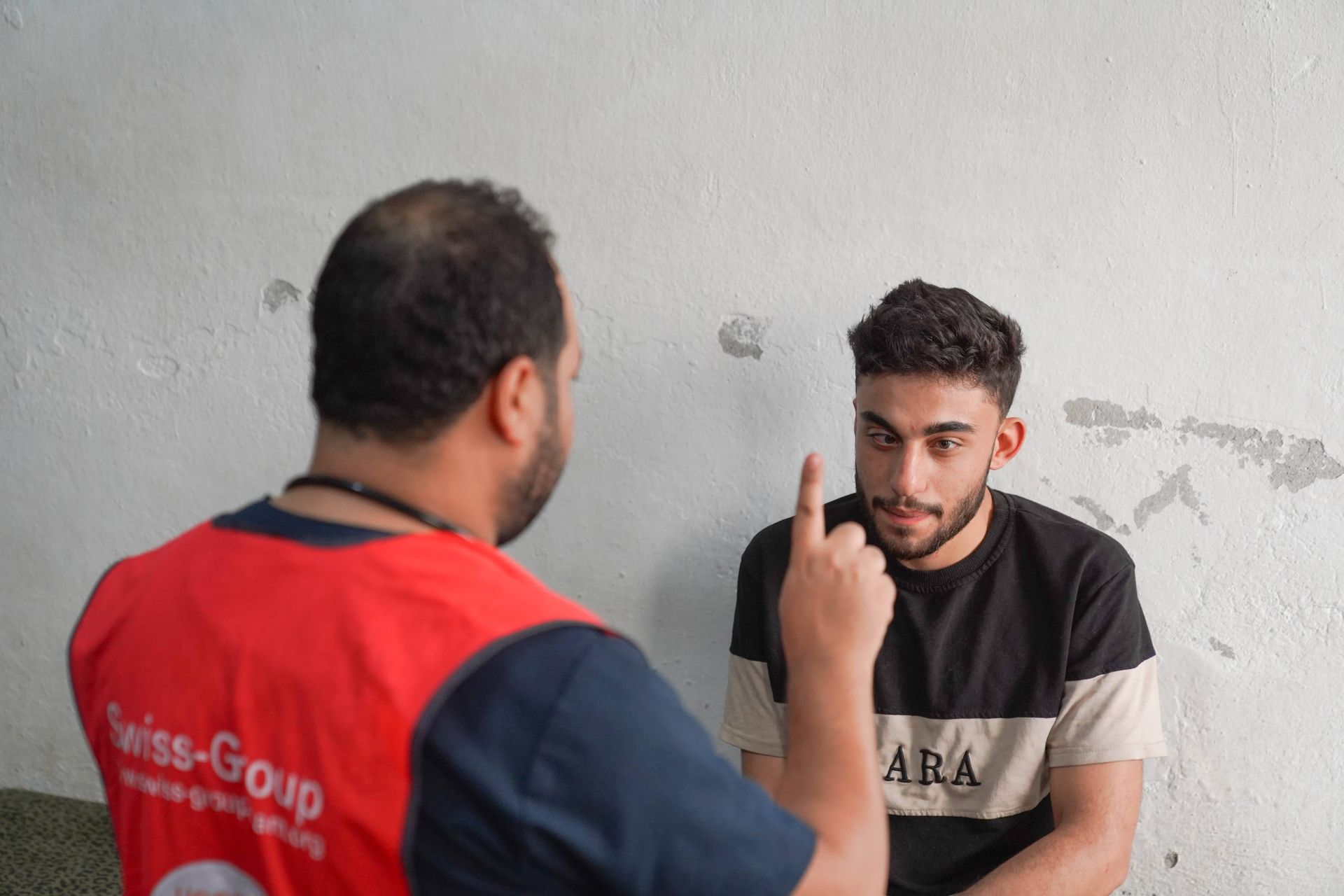 Une personne vêtue d'un gilet rouge effectue un test de suivi oculaire sur une autre personne qui regarde le doigt levé.