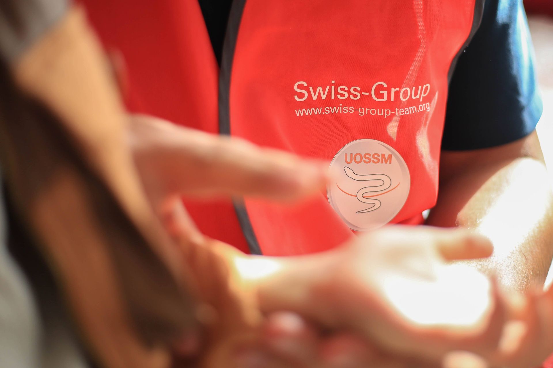 Gros plan sur une personne portant un gilet orange haute visibilité du groupe suisse, vérifiant les mains d'une autre personne.