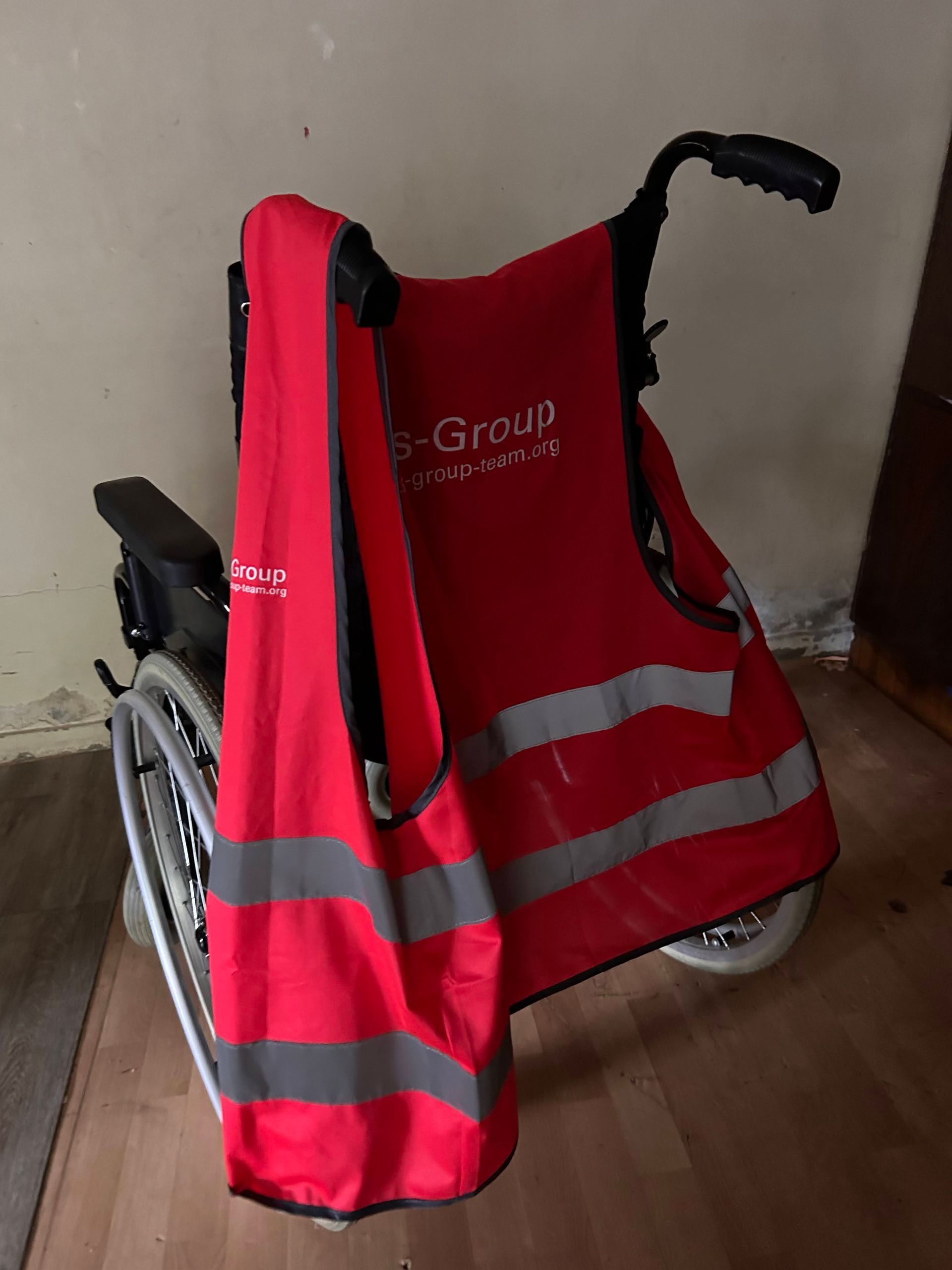 Un fauteuil roulant dans un intérieur, recouvert d'un gilet de sécurité rouge haute visibilité à bandes grises réfléchissantes.
