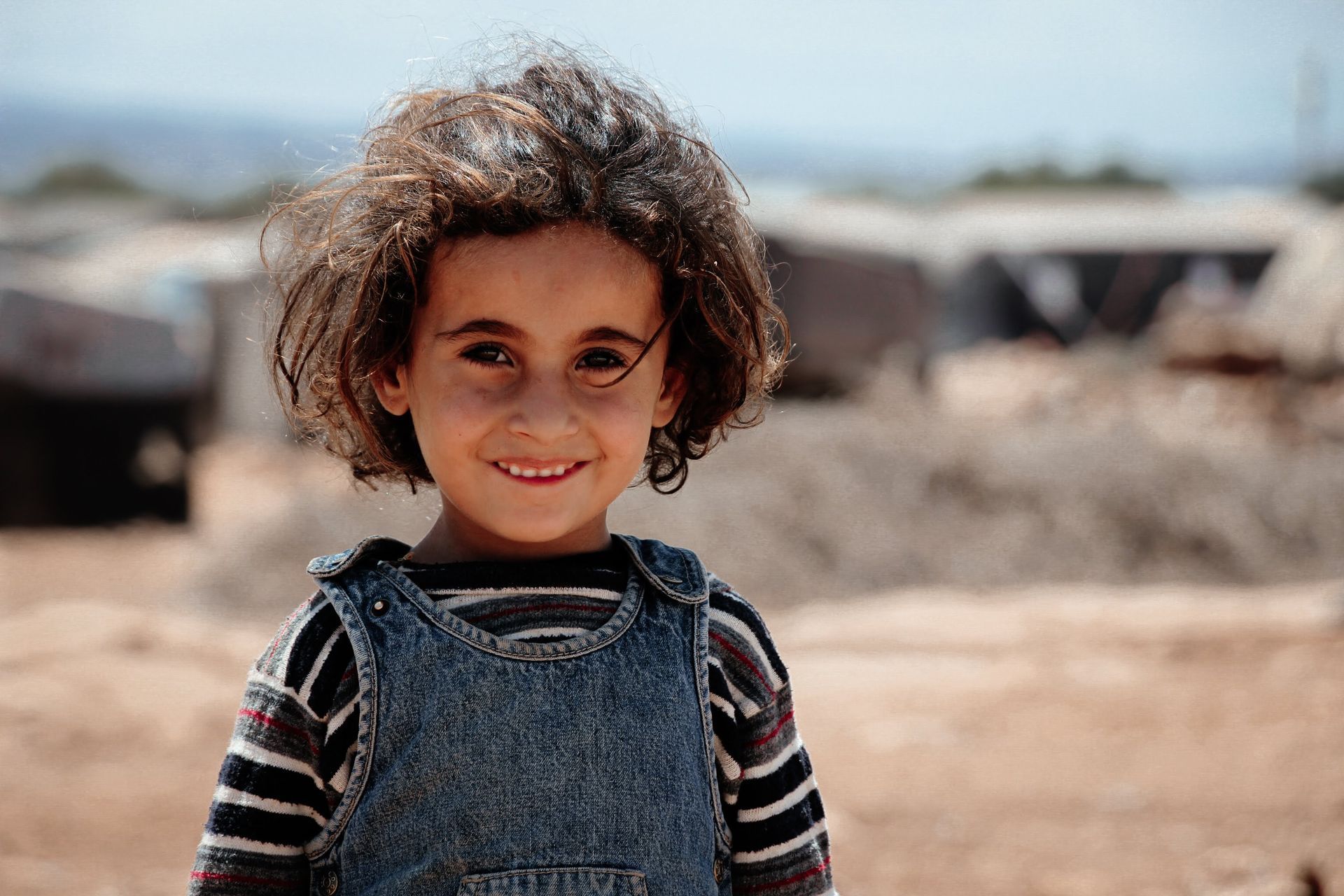 Une personne vêtue d'une robe à motifs et d'un foulard sur la tête traverse un paysage rocailleux en portant un récipient d'eau en plastique bleu vif.