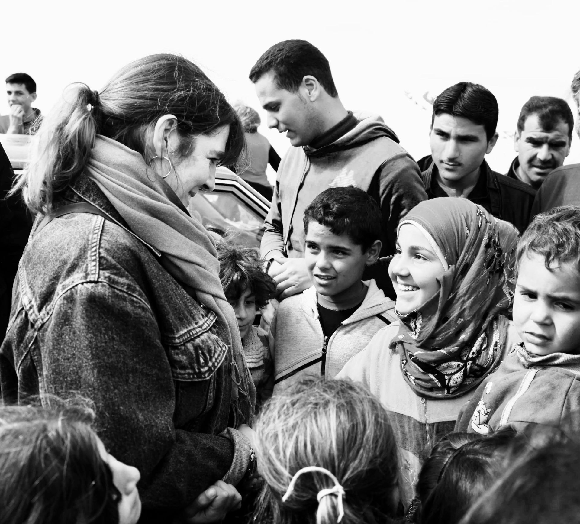 Une personne portant une veste en jean et une écharpe discute avec un groupe de personnes en extérieur.