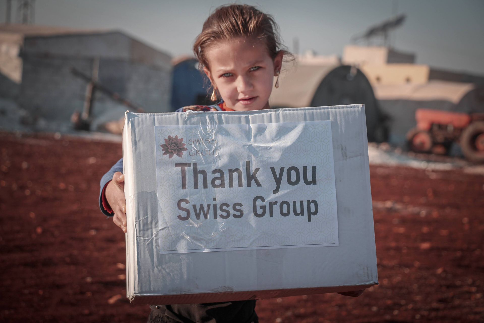 Dans un cadre rural, un enfant tient une boîte avec une pancarte sur laquelle on peut lire « Merci Swiss Group ».