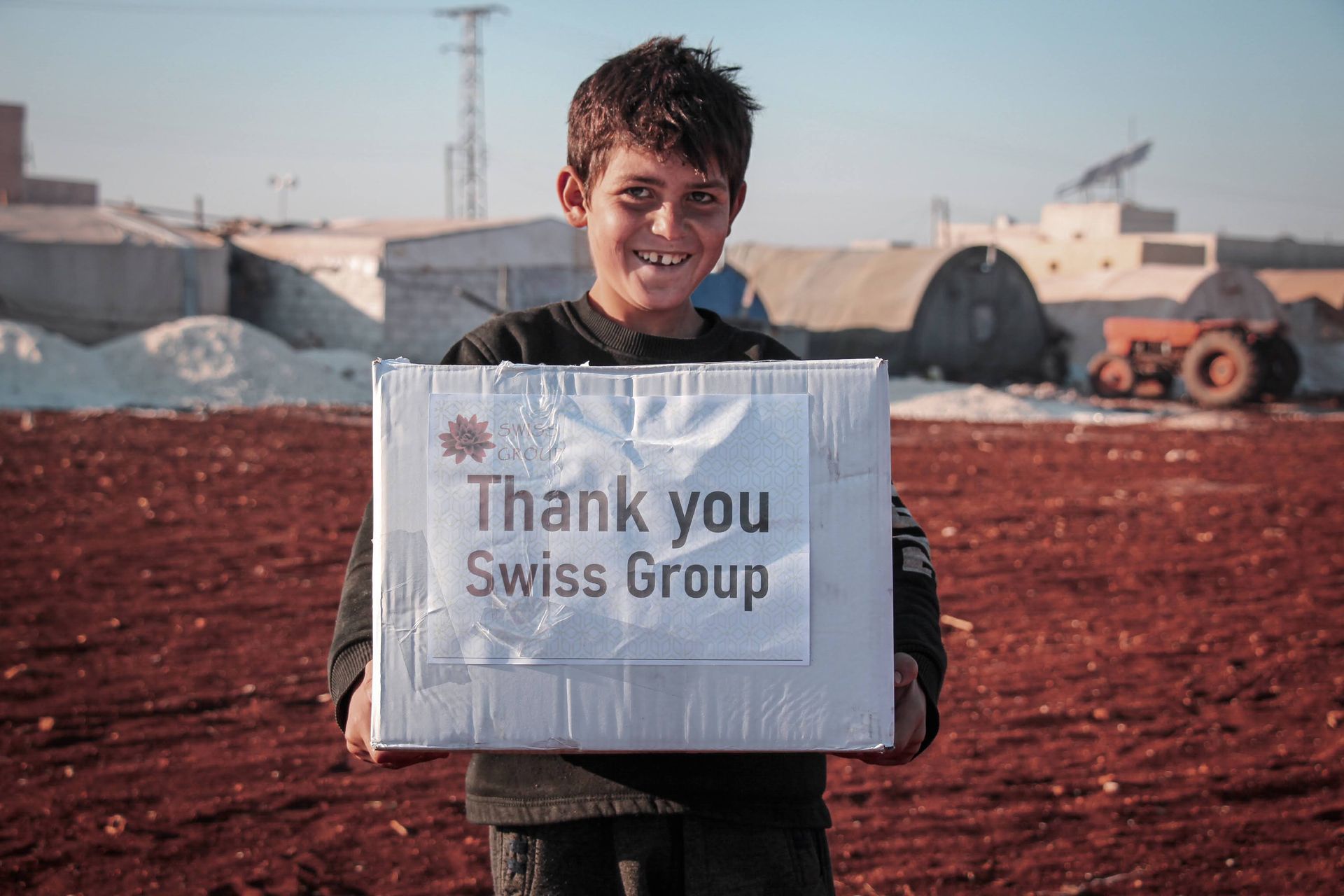 Une personne souriante tenant une boîte avec une pancarte sur laquelle on peut lire « Merci Swiss Group » dans un cadre champêtre.