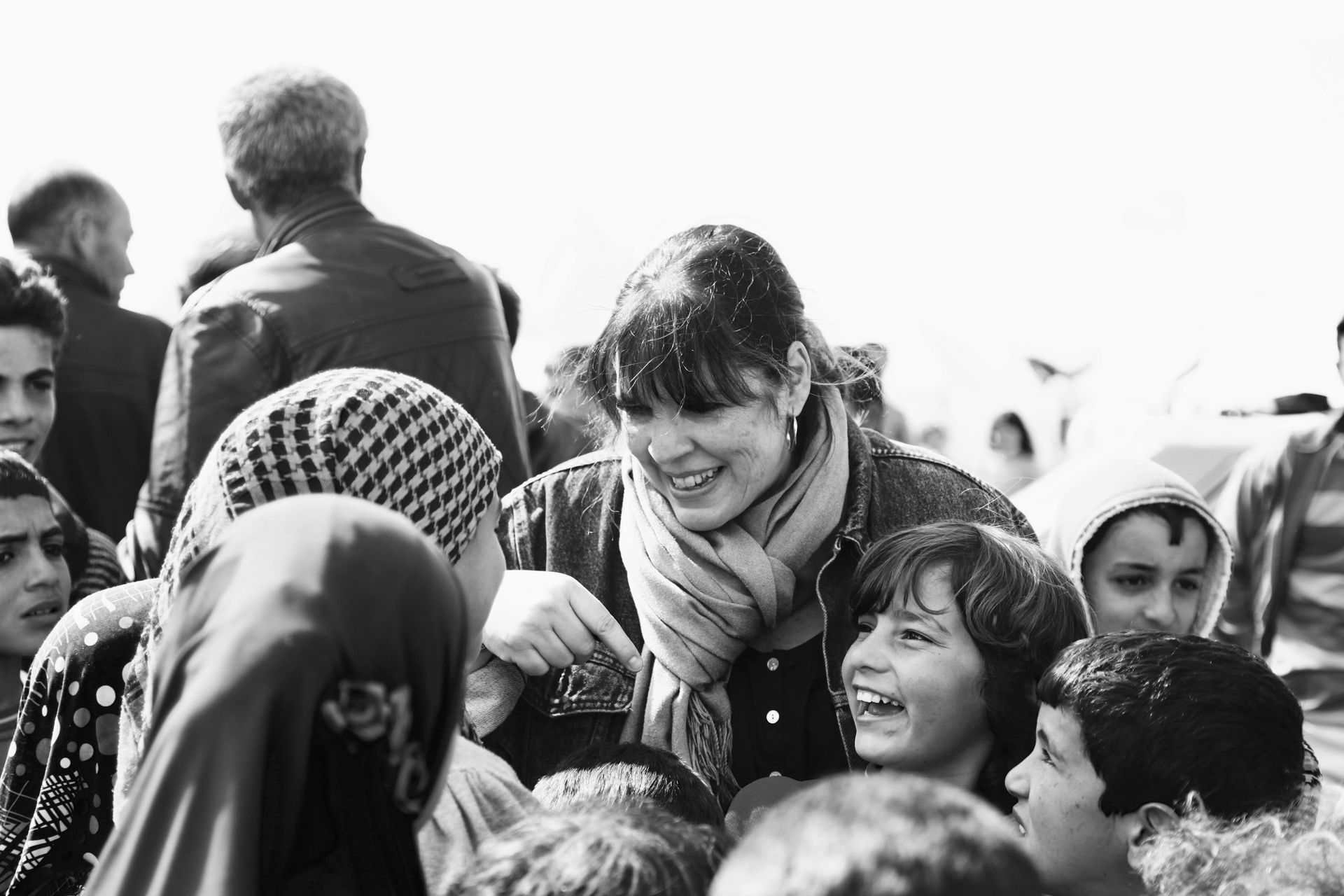Une personne souriante portant une écharpe interagit avec un groupe d'enfants dans un cadre extérieur lumineux.