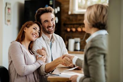 Couple shaking hands with a person, smiling, indoor setting.