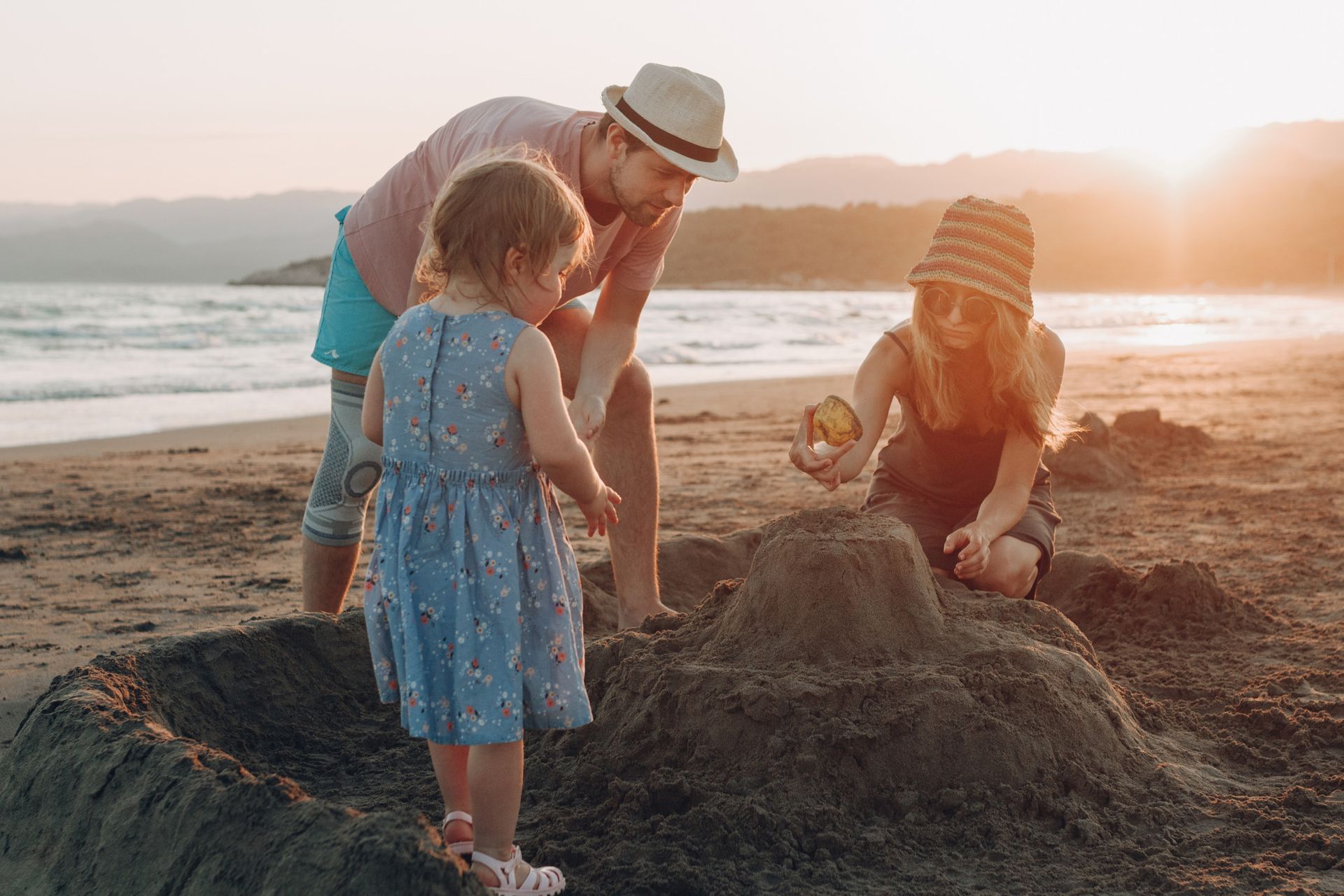 Family building a sandcastle on a beach at sunset.