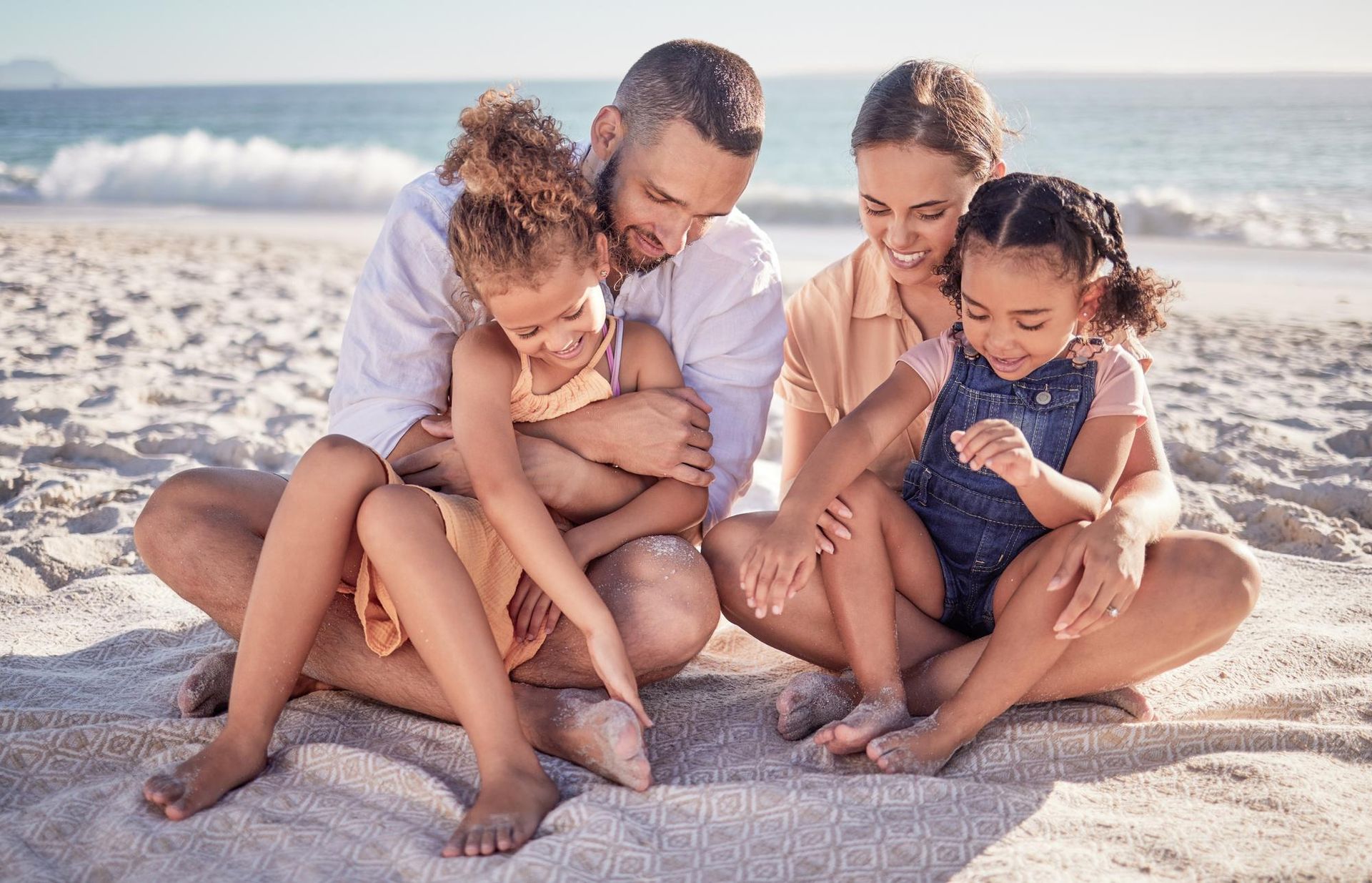 Family of four smiling on a sunny beach, looking at something on the sand.