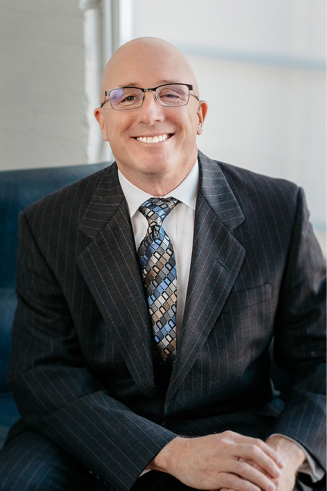 Man in suit and tie smiling, seated, indoors.