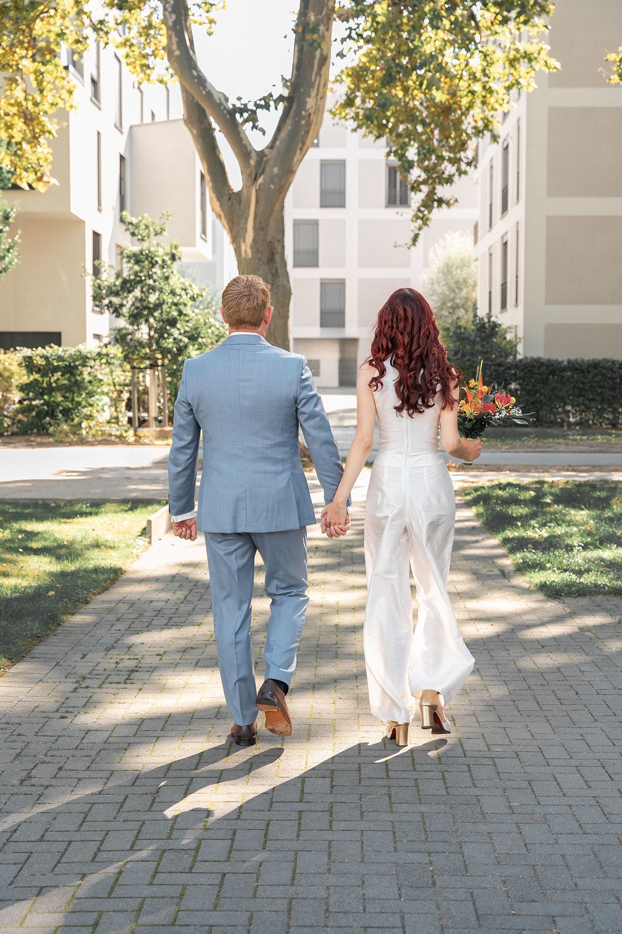 Braut und Bräutigam spazieren Hand in Hand in einem Wohngebiet in Bad Kreuznach von der Kamera weg