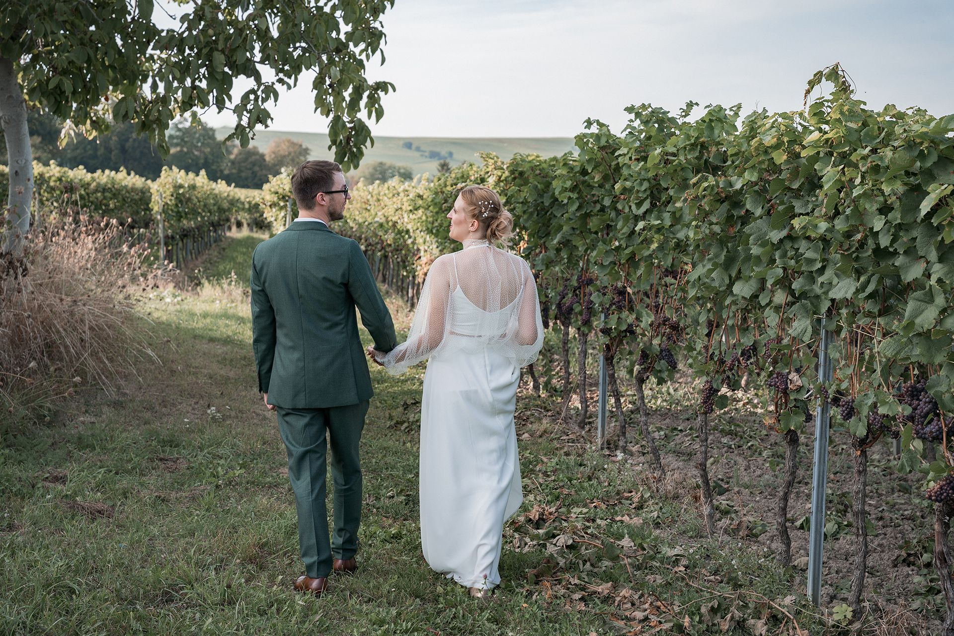 Brautpaar läuft in den Weinbergen, Rücken zur Kamera für Hochzeitsfotos in Bodenheim