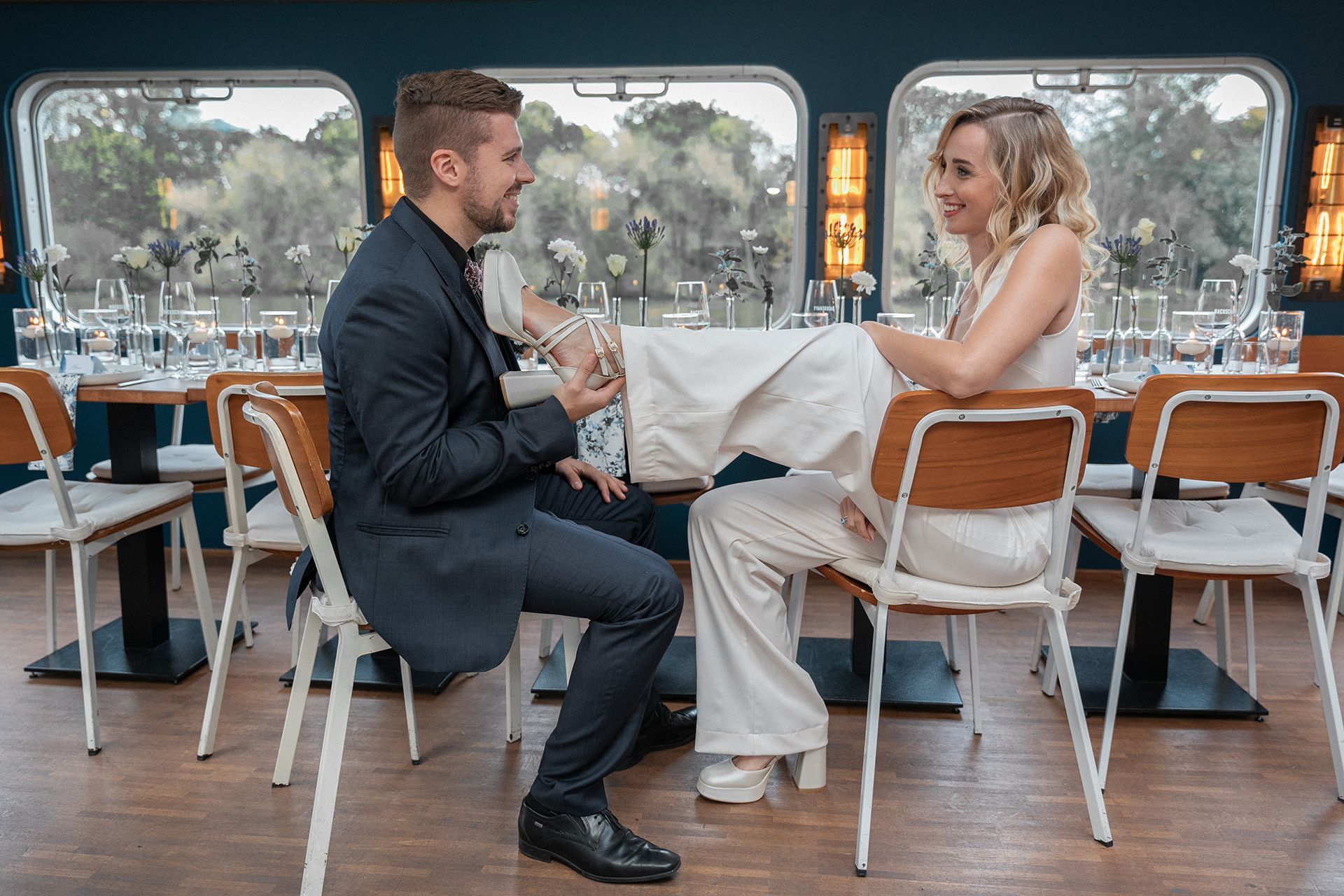 Brautpaar in Frankfurt sitzt sich gegenüber, sie streckt ihm Fuß hin, er hält ihn am Absatz fest, beide lächeln