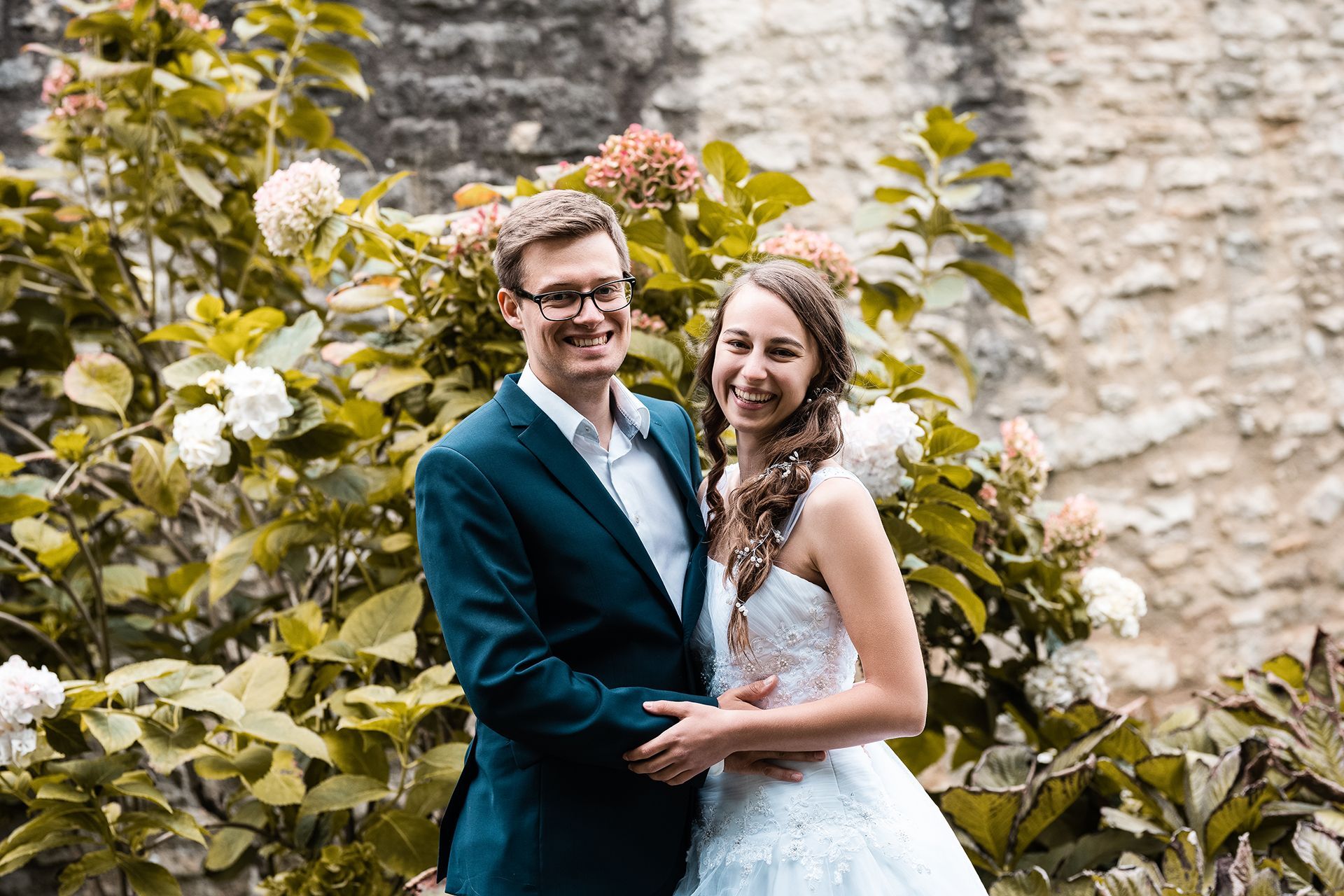 Brautpaar vor Hortensienbusch, hält Händchen und lacht in die Kamera – Hochzeitsfotos Mainz