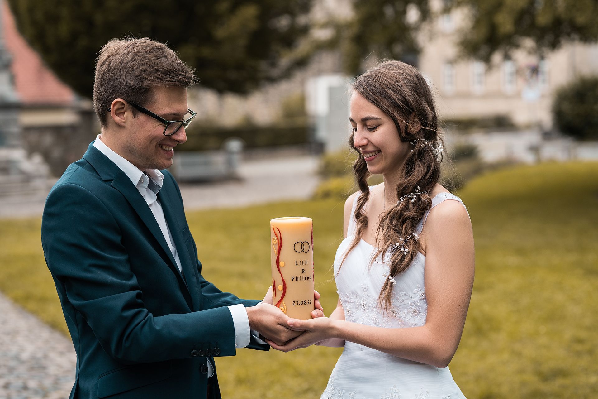 Braut und Bräutigam halten Traukerze, schauen freudig darauf – Mainzer Stadtpark im Hintergrund