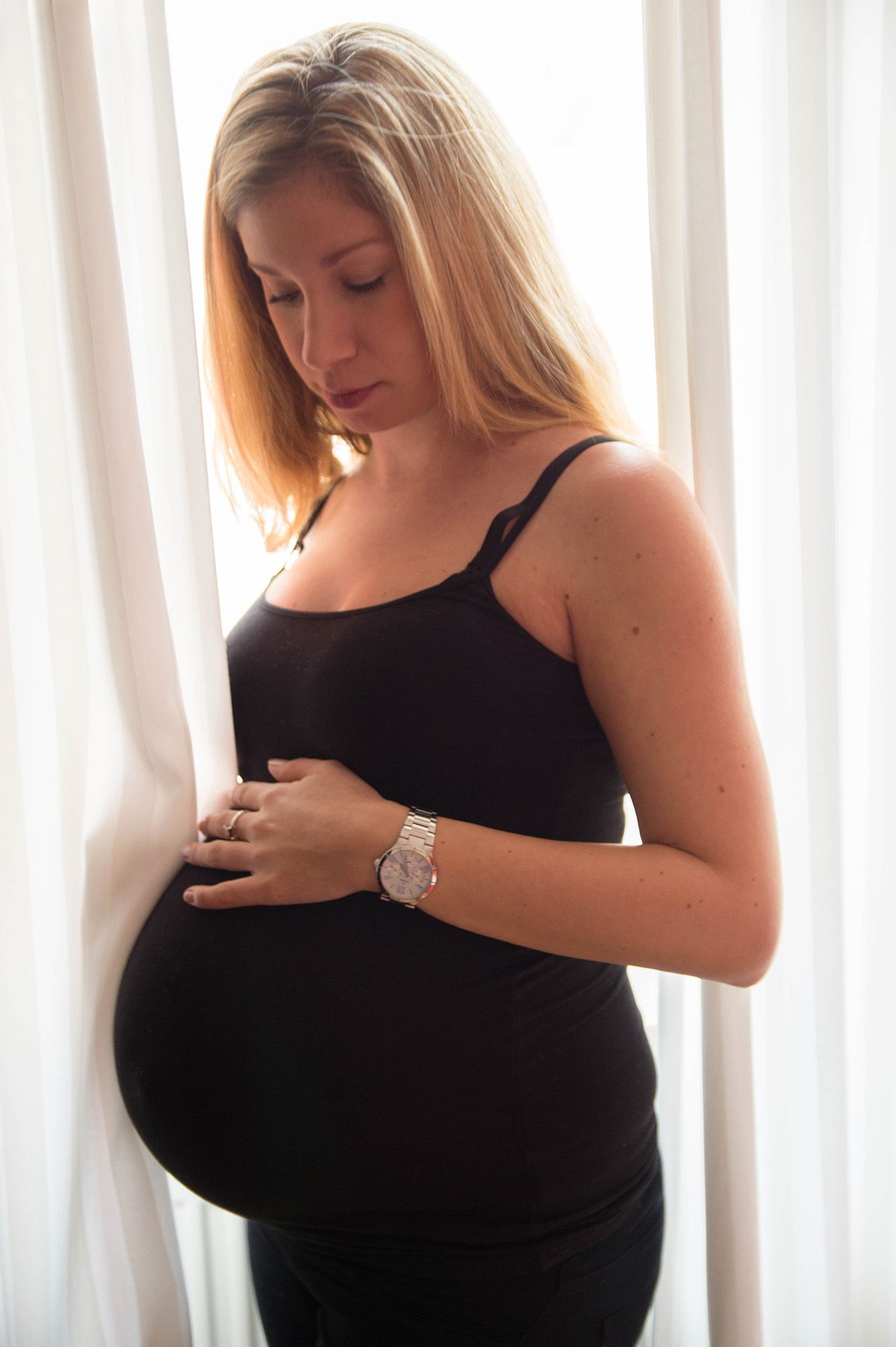 Werdende Mama steht am Fenster und schaut auf ihren Babybauch zu Hause in Mainz