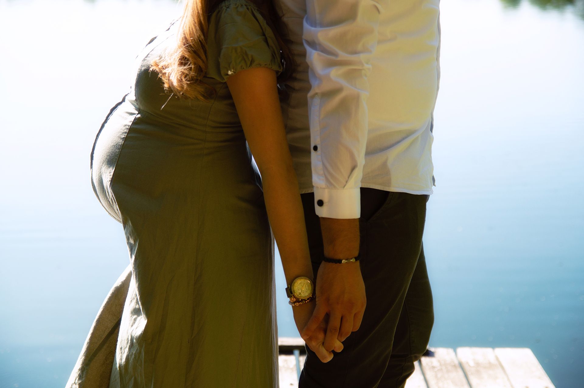 Paar Rücken an Rücken am Wasser mit sichtbarem Babybauch in Ingelheim