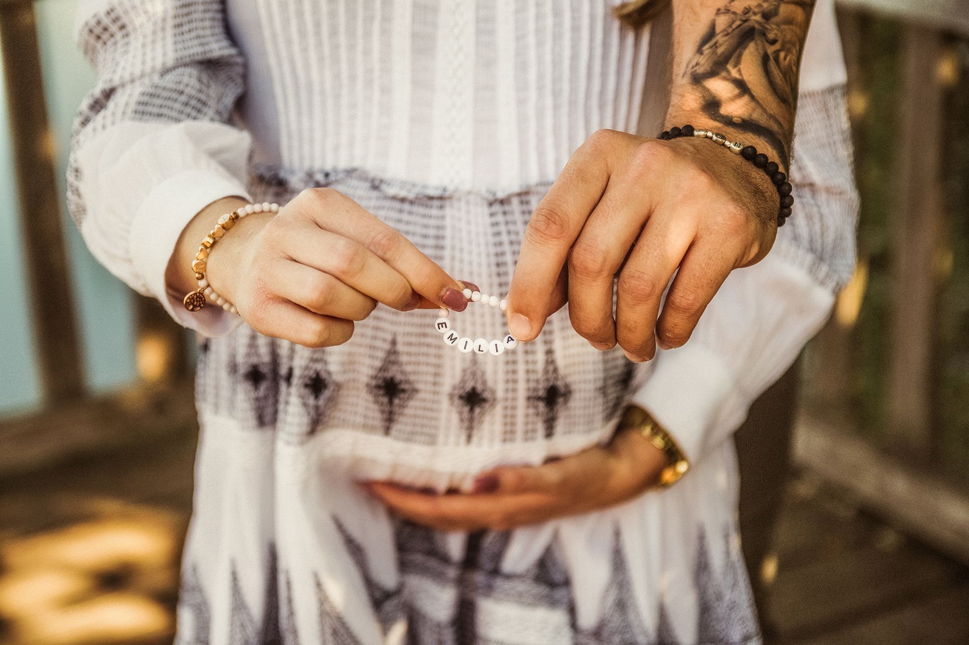 Babybauch Shooting Ingelheim - Babybauch im Fokus, sie hält Armband mit Namen, er hält ihren Babybauch fest 
