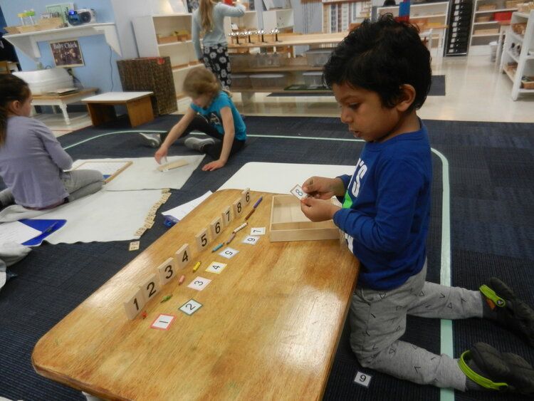 A boy in a blue shirt is kneeling at a table with numbers on it