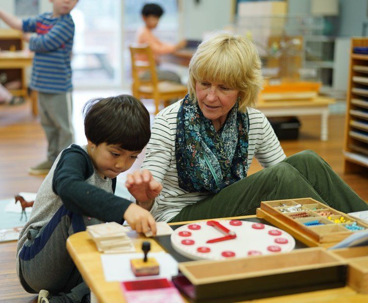 A woman sits at a table with a child playing with a clock