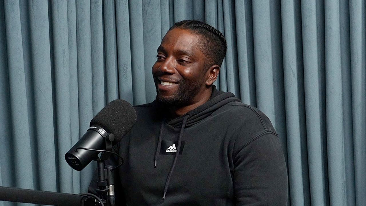 A man in a black hoodie is sitting in front of a microphone.