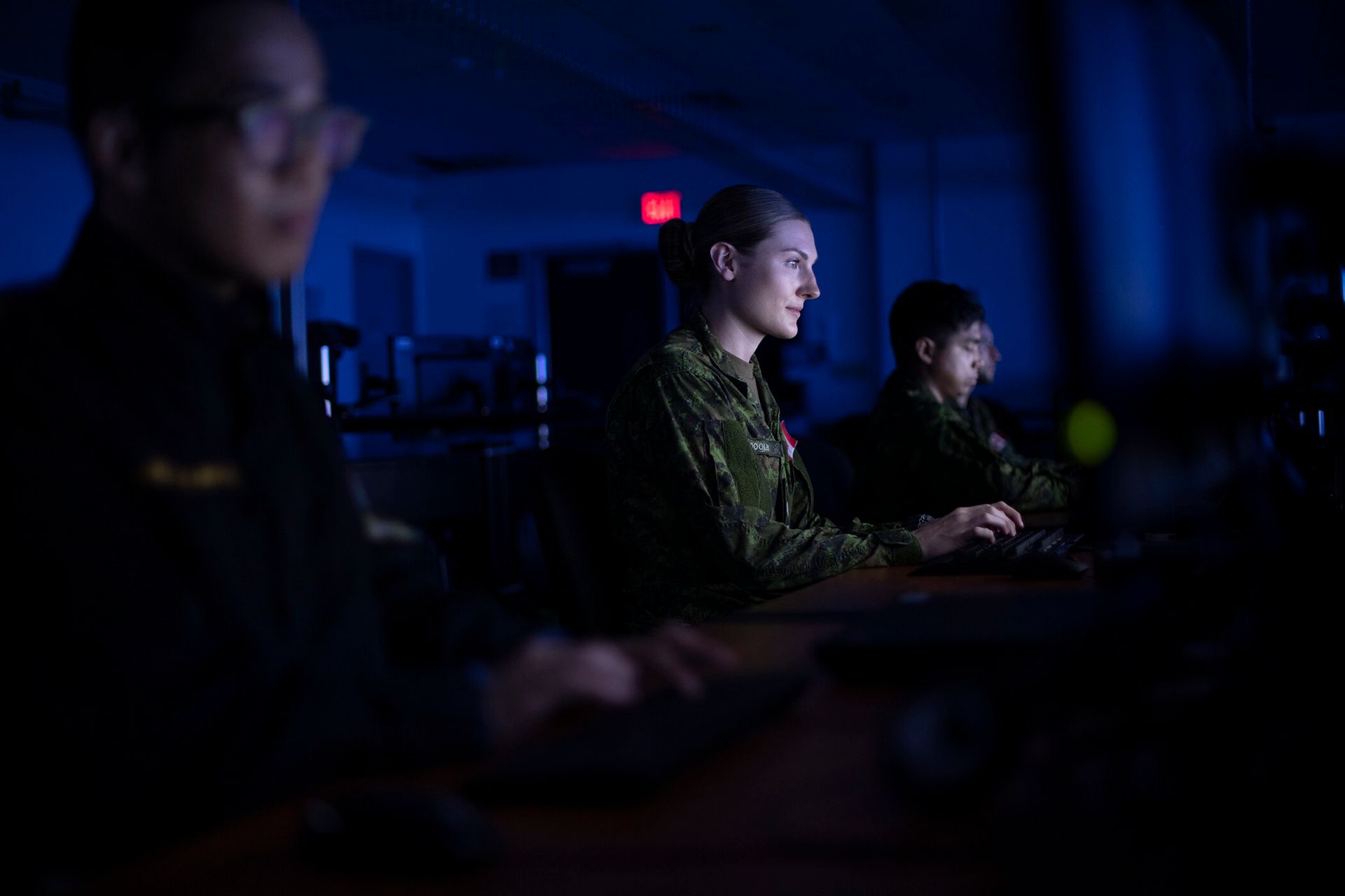 A group of soldiers are sitting in front of a computer screen in a dark room.