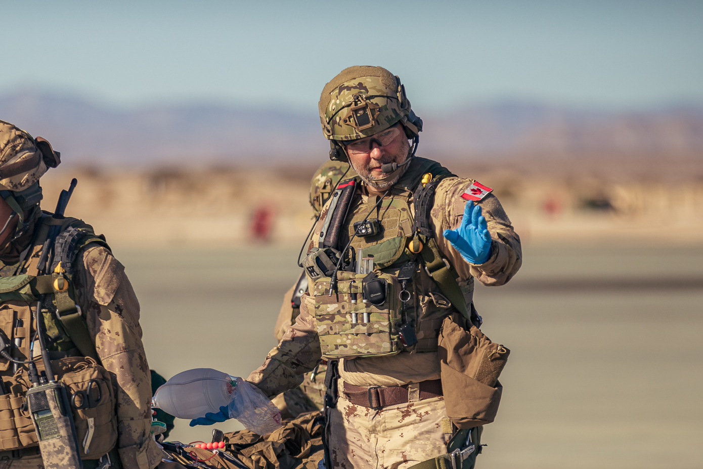Two soldiers are walking in the desert carrying a stretcher.