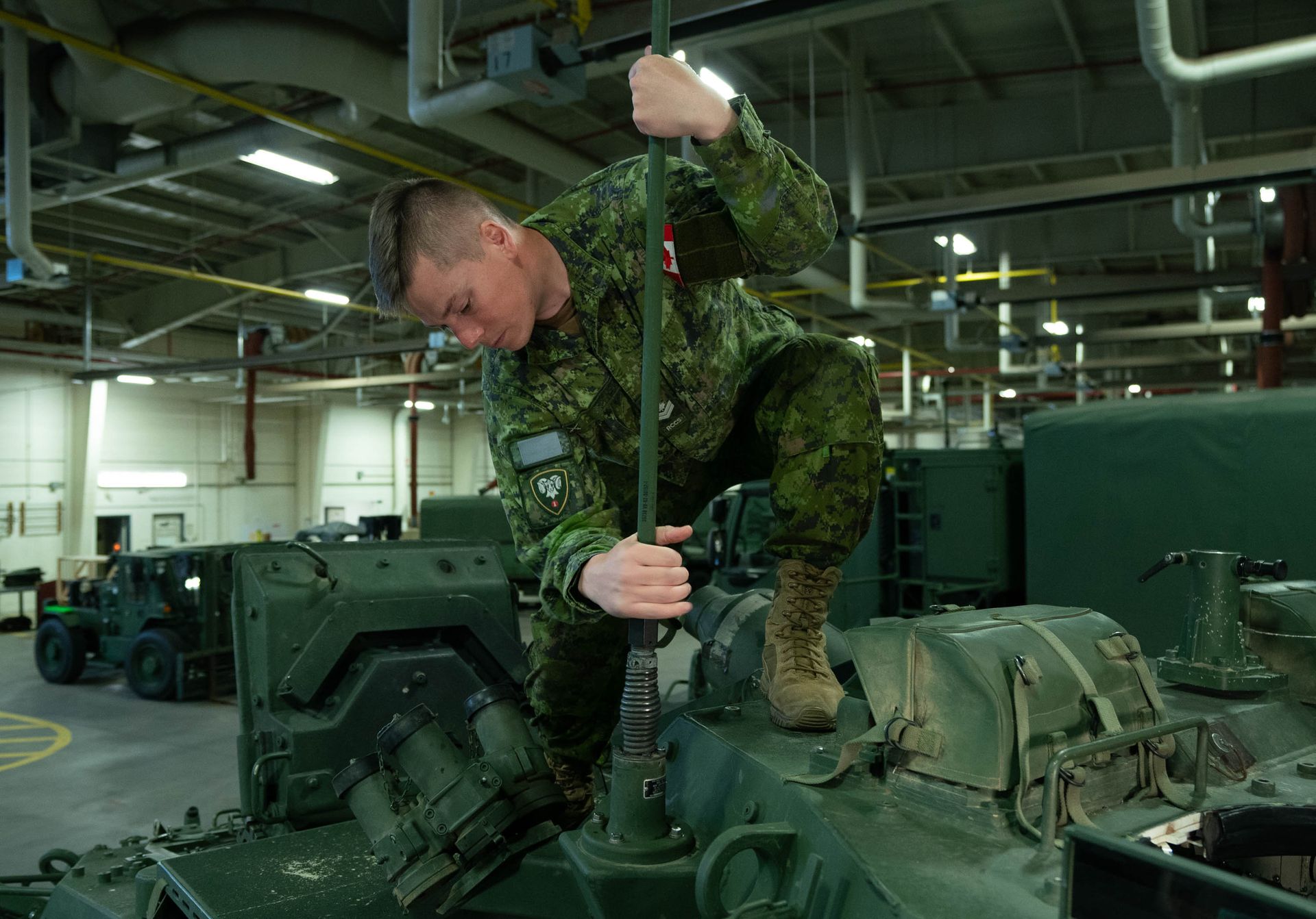 A soldier is working on a tank in a warehouse.