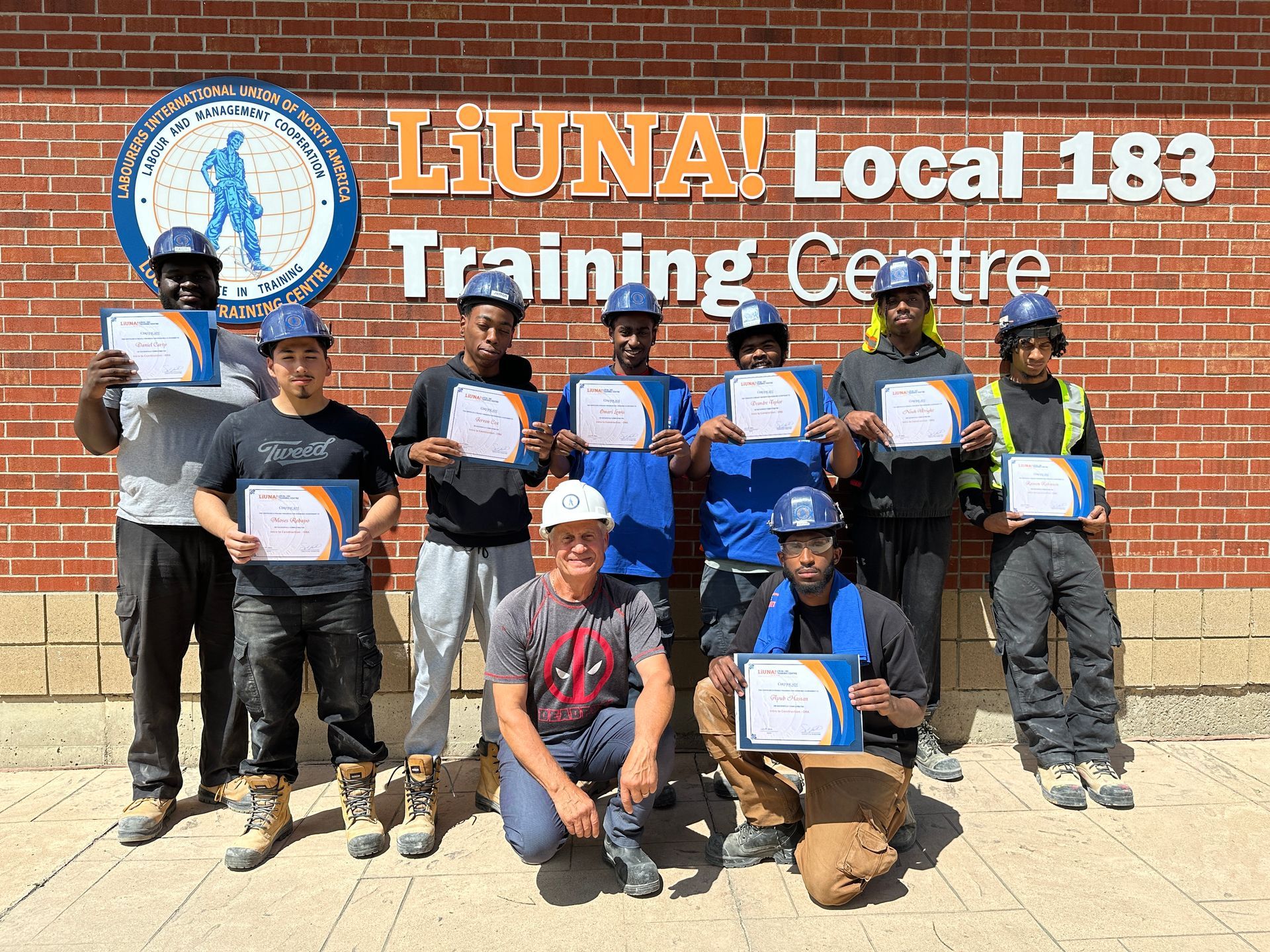 A group of construction workers are posing for a picture in front of a brick building.