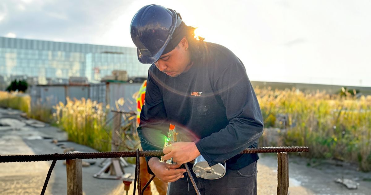 A man wearing a hard hat is tying a piece of metal.