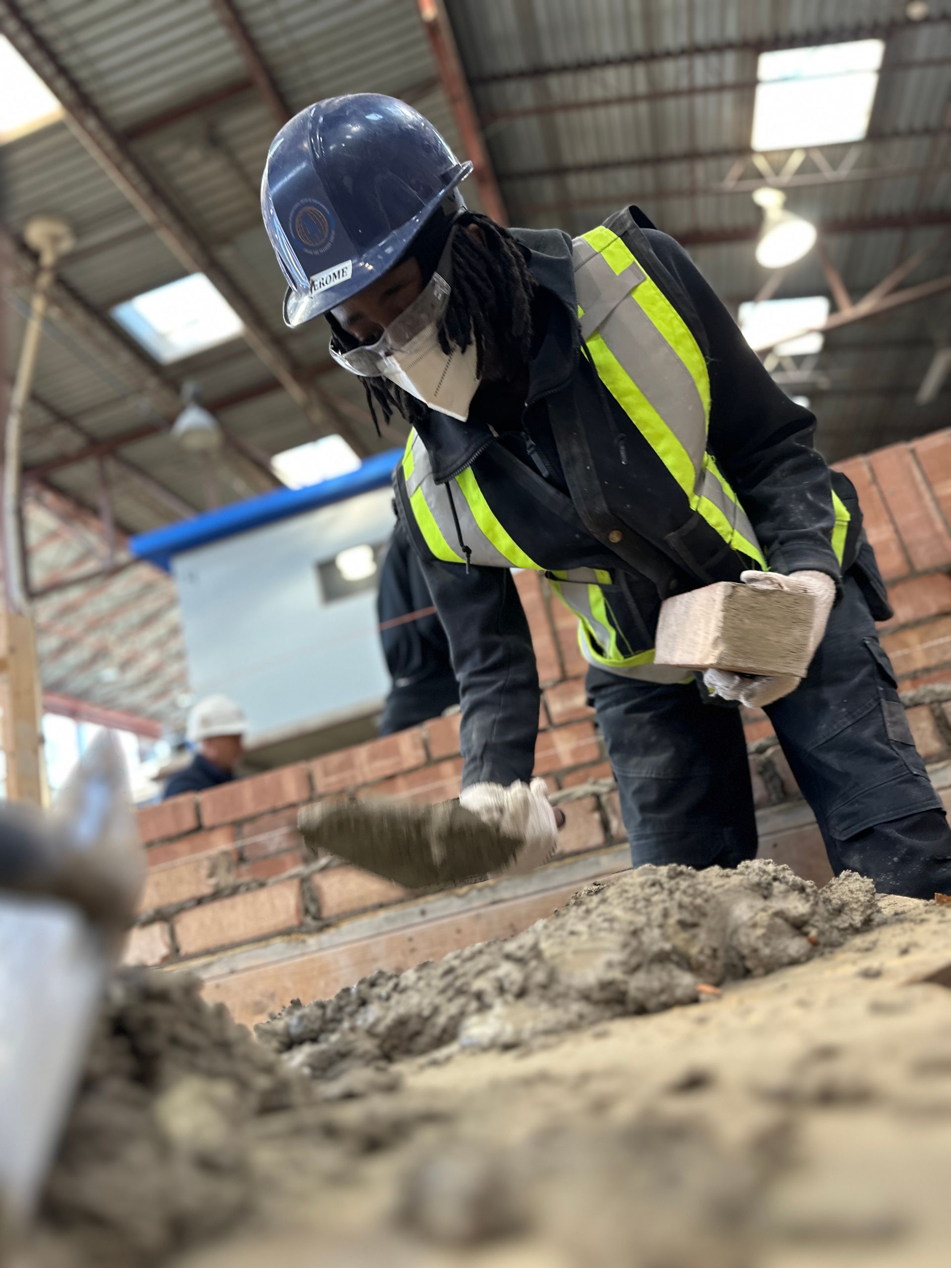 a man wearing a hard hat and safety vest is working on a brick wall