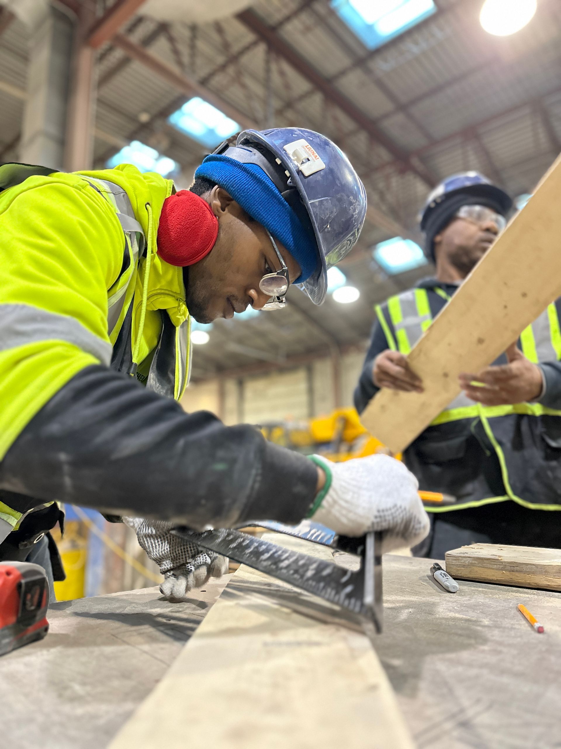 a man wearing a hard hat is cutting a piece of wood .