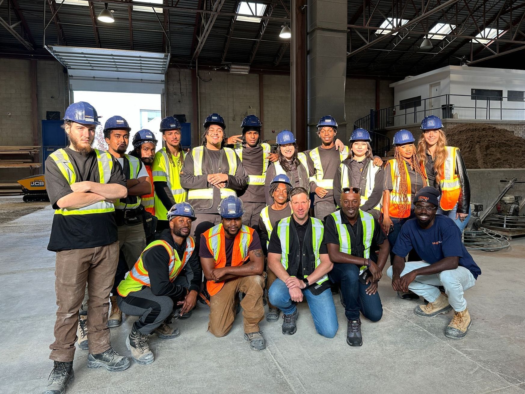 A group of construction workers are posing for a picture in a warehouse.