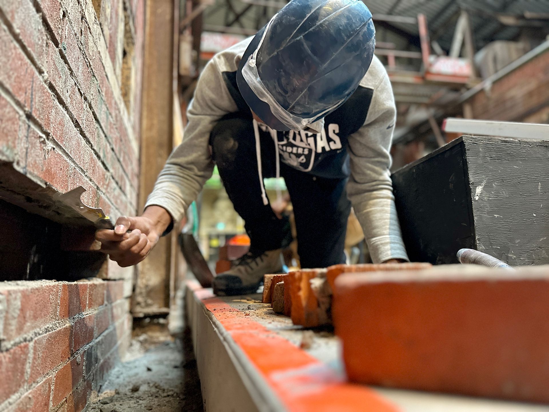 A man wearing a hard hat is working on a brick wall.