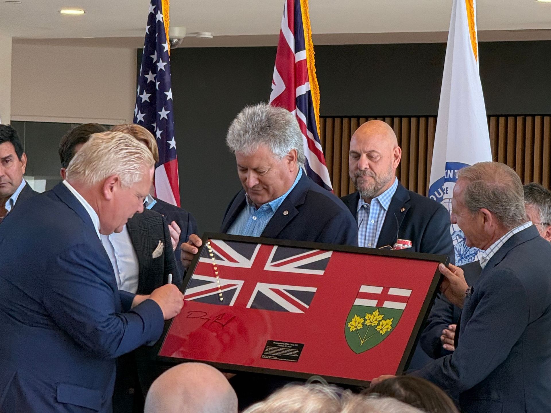 A group of men are holding a framed flag in front of flags.