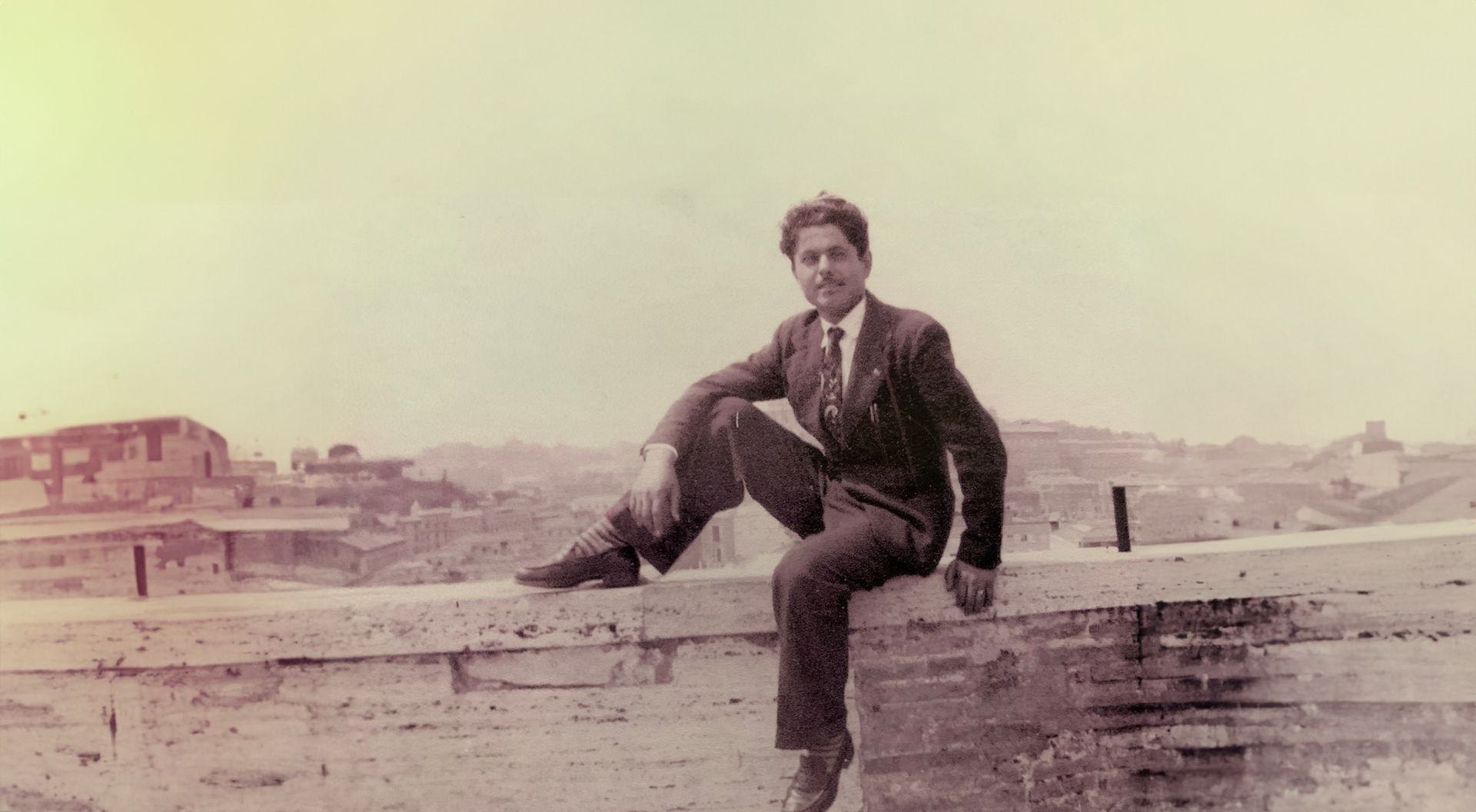 A man in a suit and tie is sitting on a wall.