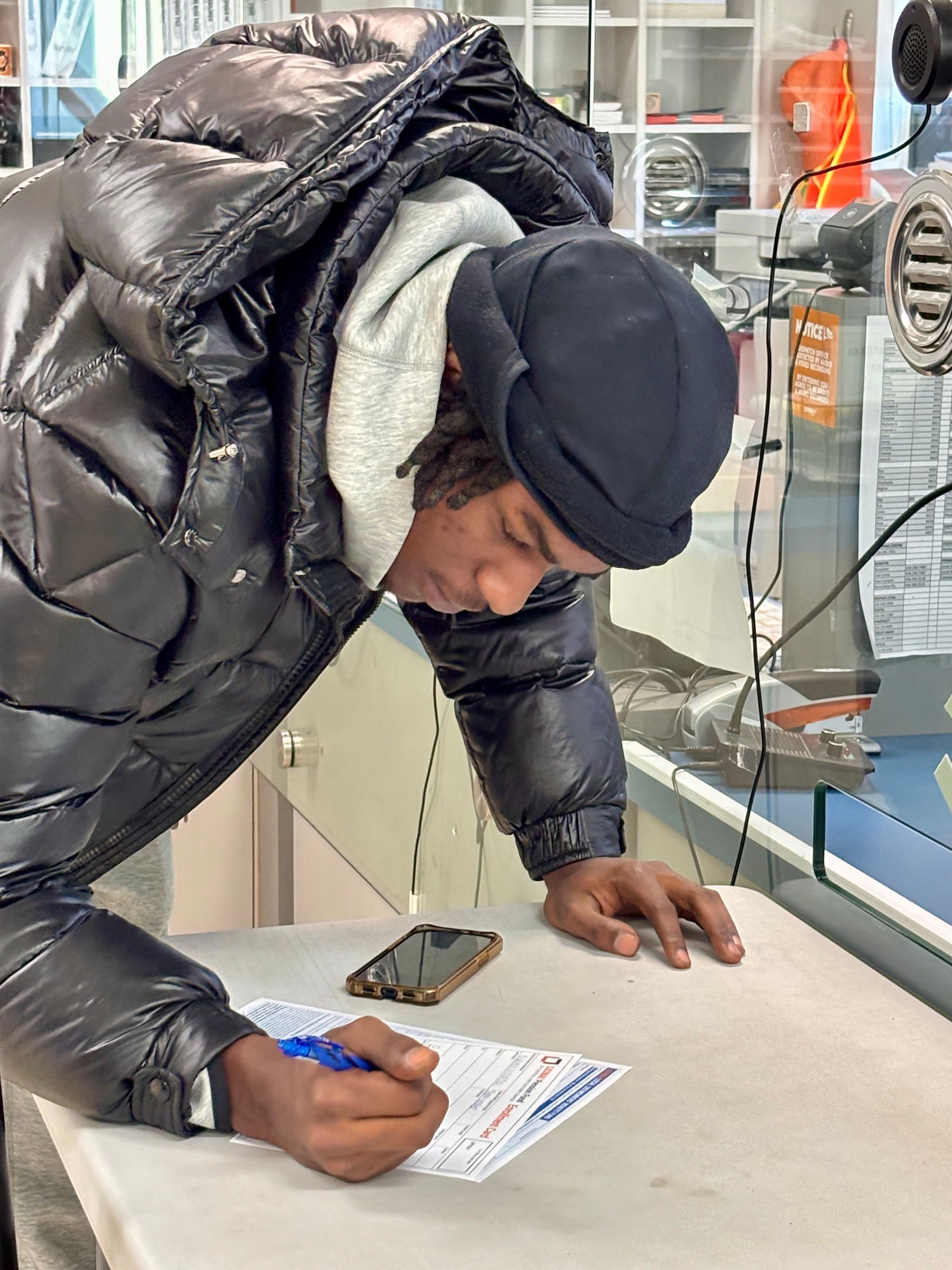 A man in a black jacket is writing on a piece of paper.