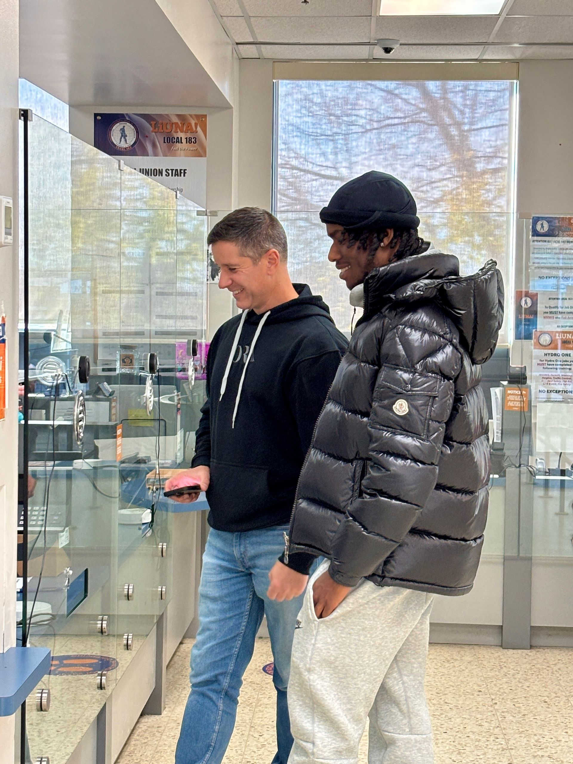 Two men are standing next to each other in a store . one of the men is wearing a black jacket.