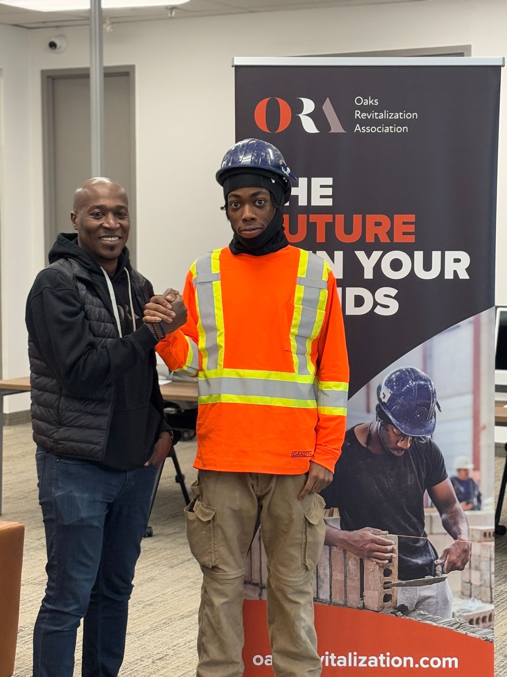 Two men are shaking hands in front of a sign that says the future in your hands