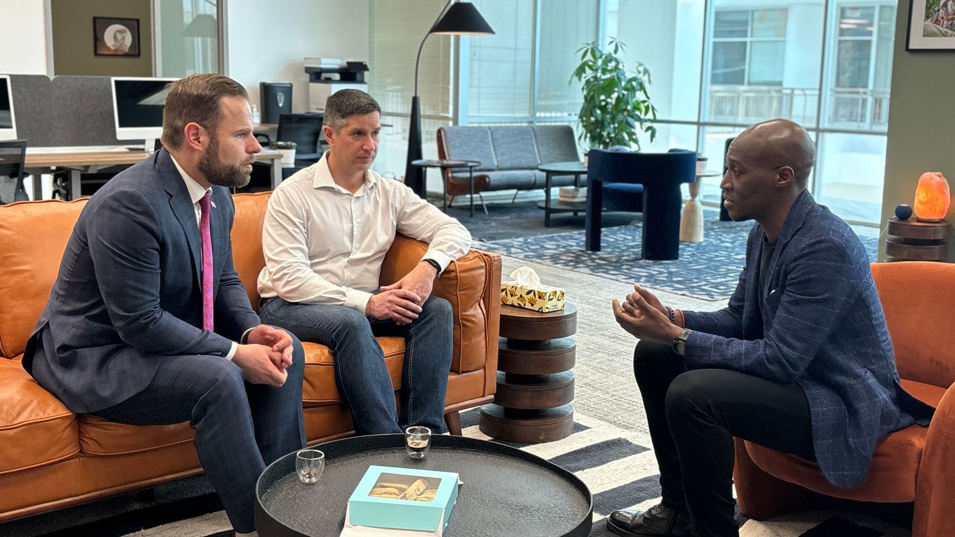 Three men are sitting on a couch talking to each other.