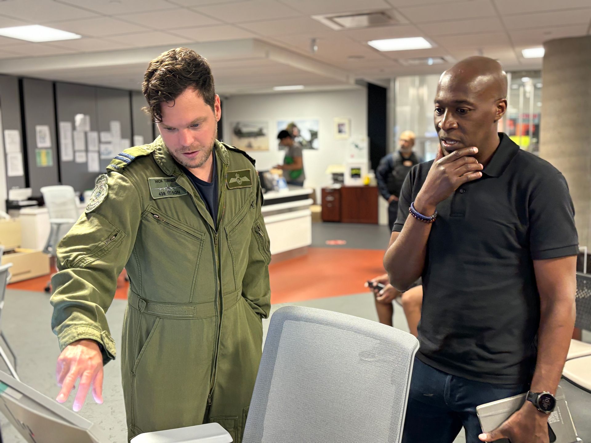 A man in a military uniform is standing next to a man in a black shirt.