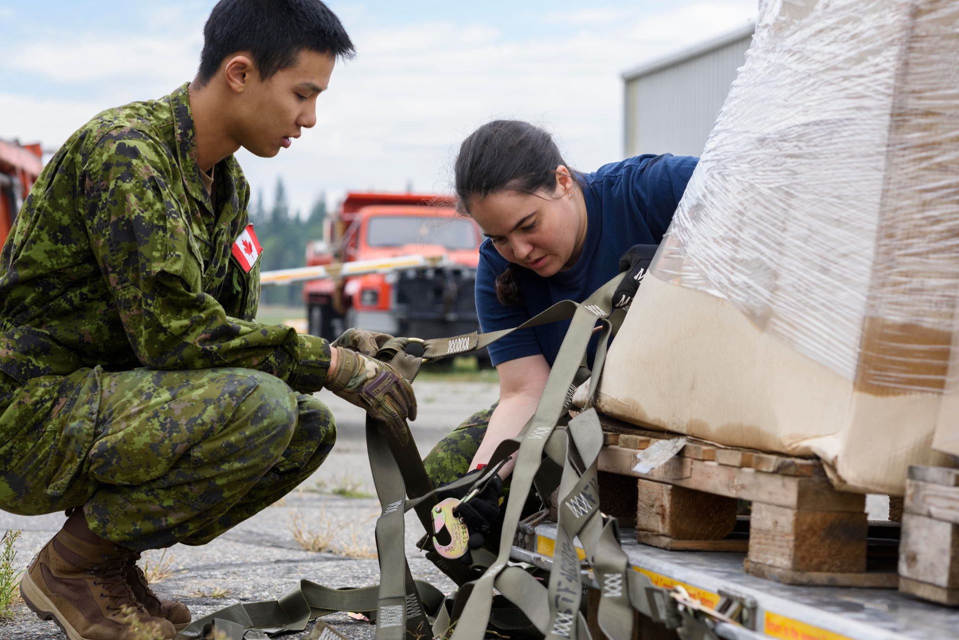 A man and a woman in military uniforms are working on a truck.