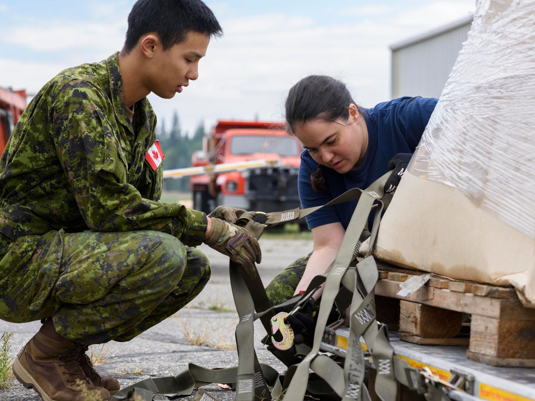 A man and a woman in military uniforms are working on a trailer.