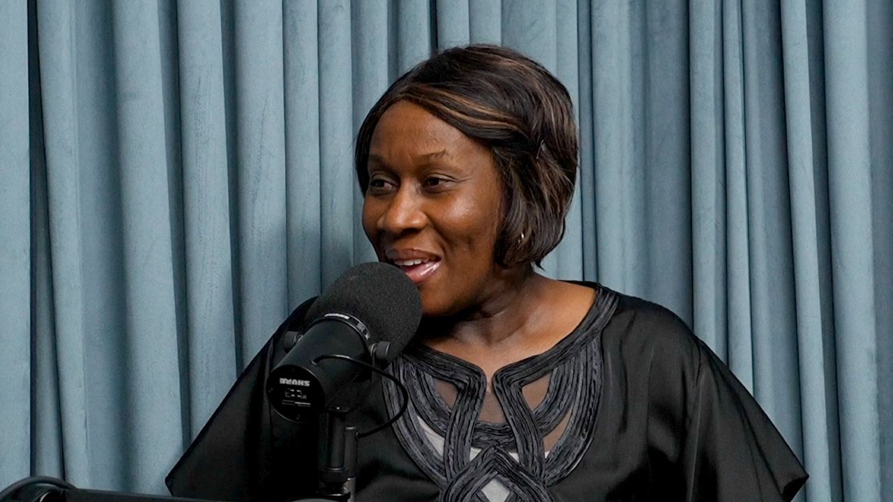 A woman is talking into a microphone in front of a blue curtain.