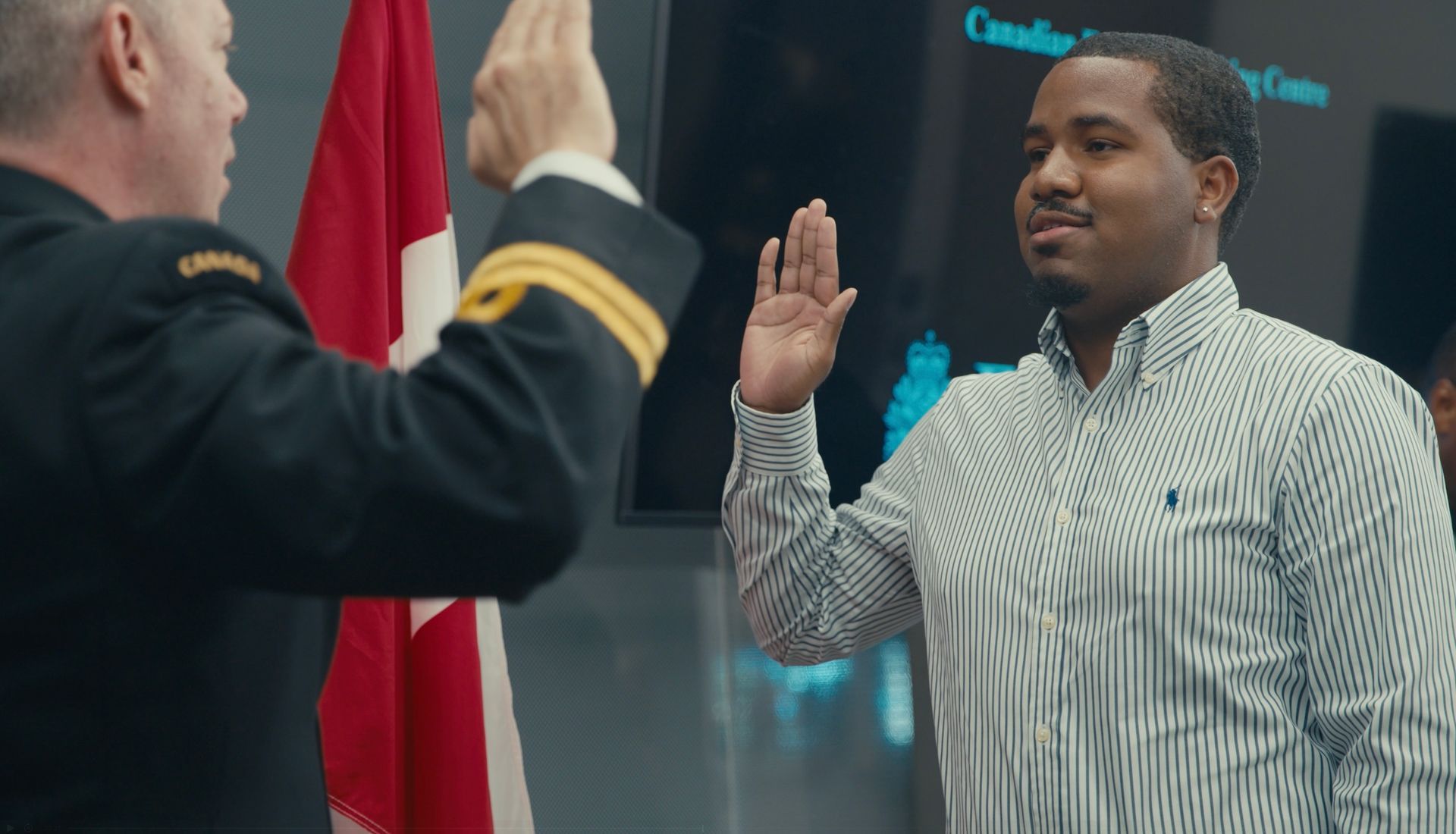 Man taking an oath, raising hand in front of a Canadian flag, indoors.