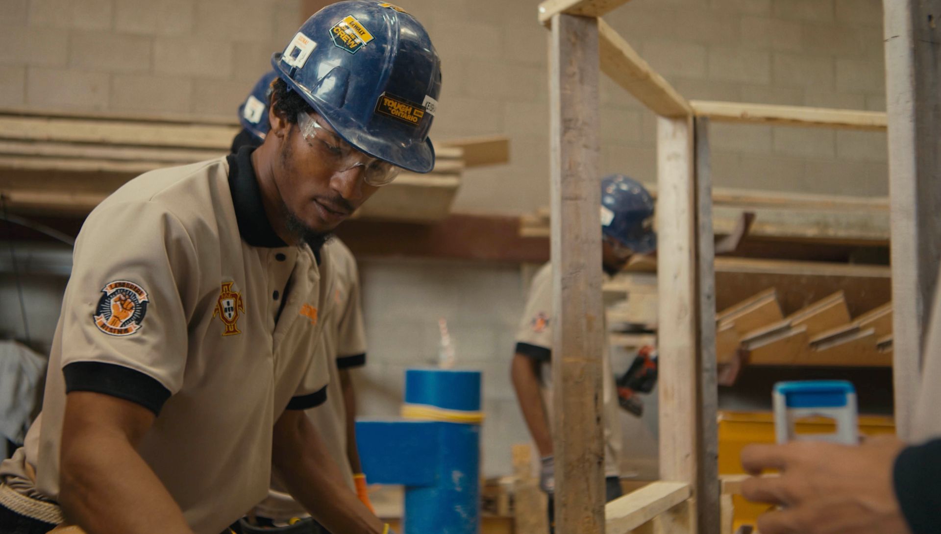 A man wearing a hard hat and safety glasses is working on a piece of wood.