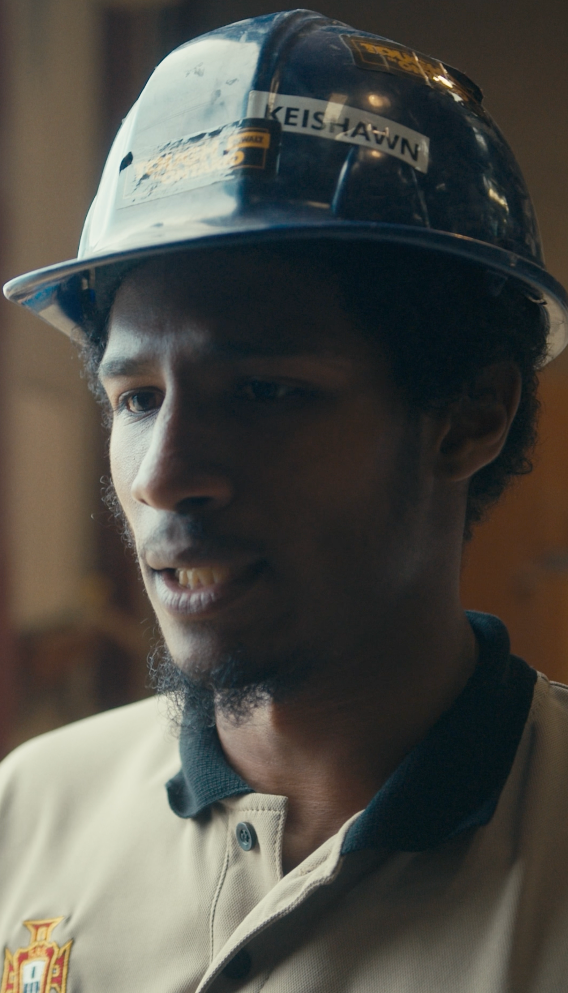 A man wearing a work hat with "KEISHAWN" on it, looking slightly concerned. He's in a work setting, possibly indoors.