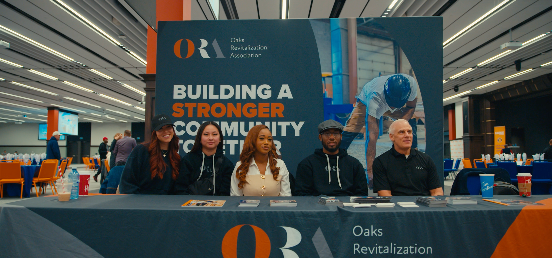 Five people seated behind a table with a sign that reads,