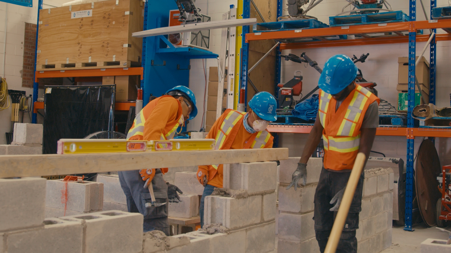 Construction workers building a cinder block wall, using a level. Indoor setting with equipment and storage. Construction workers building a cinder block wall, using a level. Indoor setting with equipment and storage.