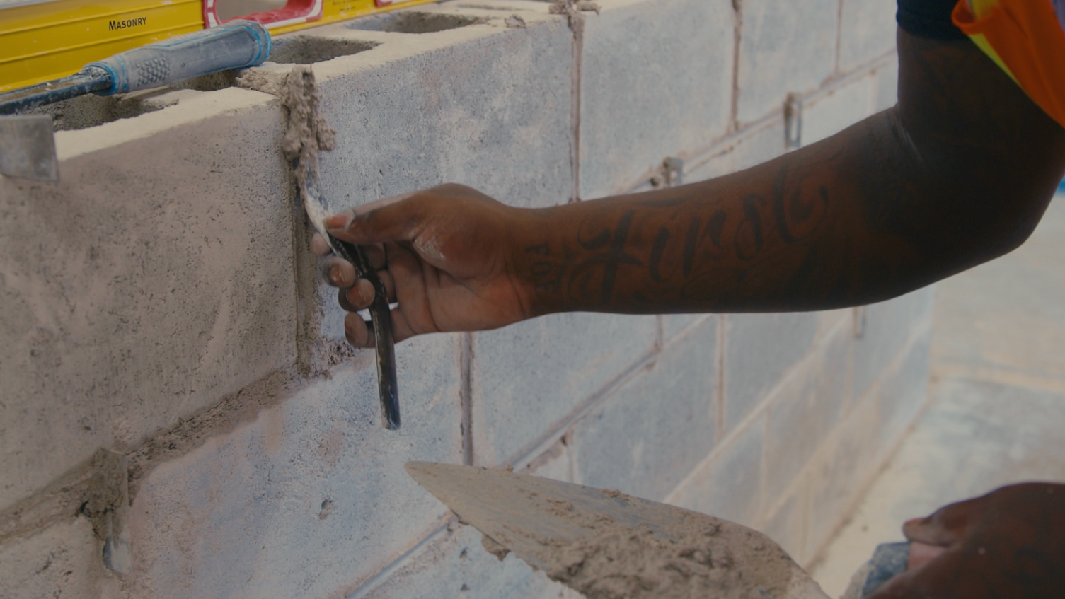 Person using a trowel to apply mortar on cinder blocks.