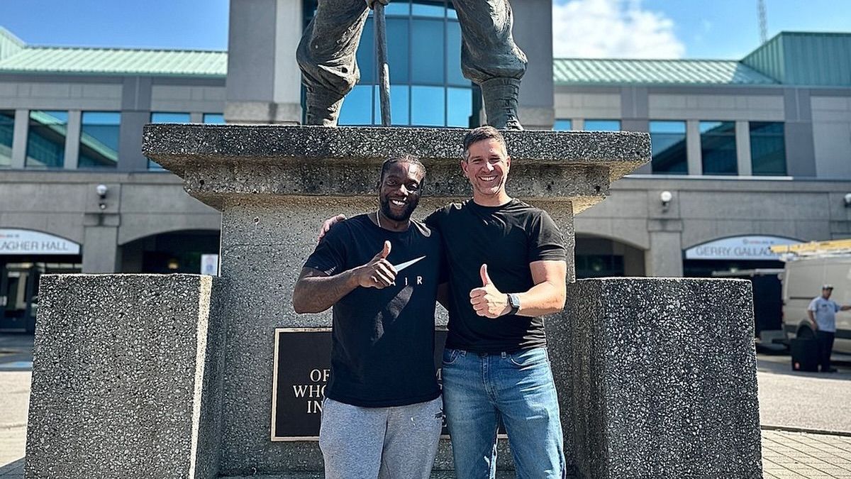 Two men are standing in front of a statue and giving a thumbs up.