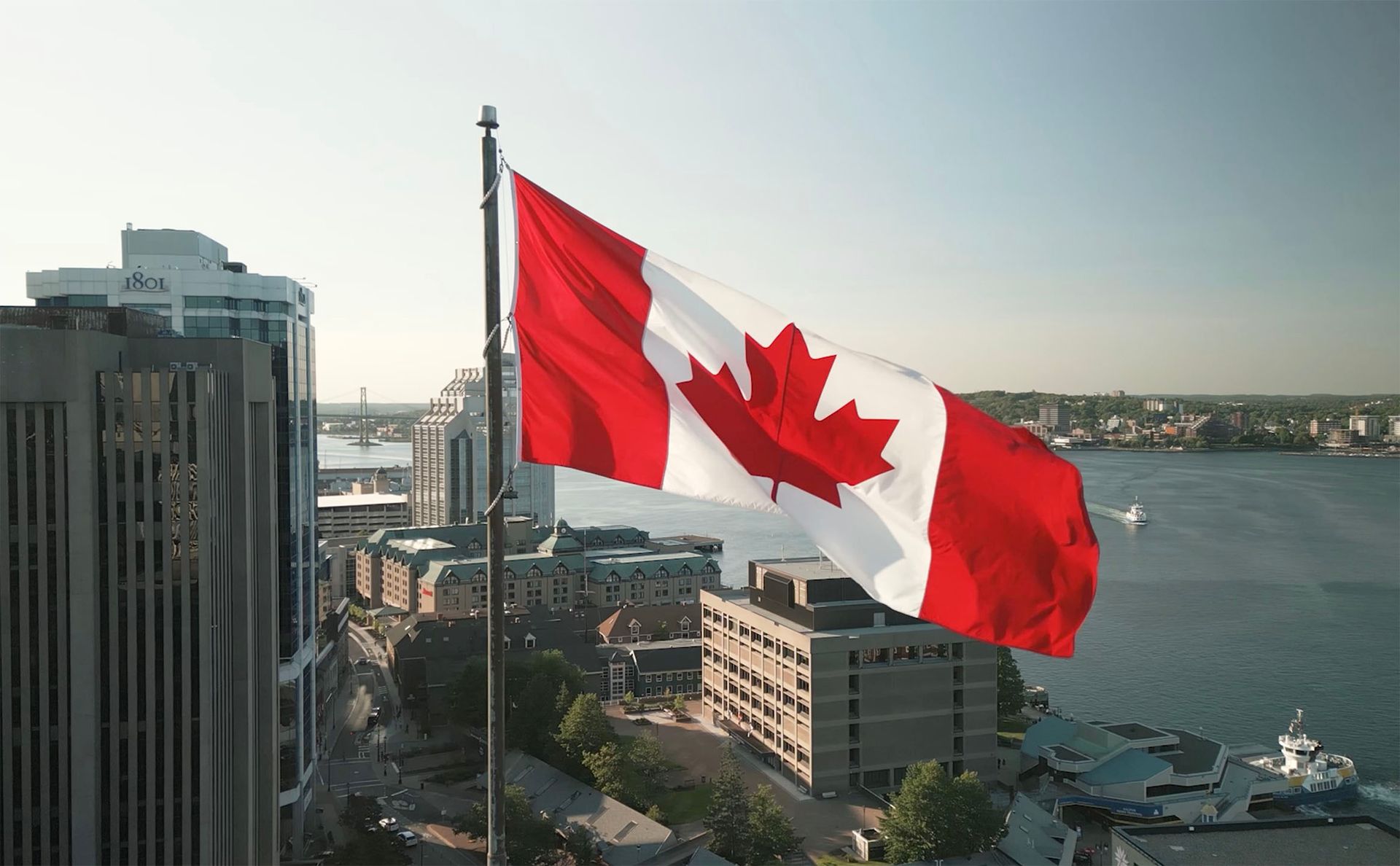 A large canadian flag is waving in the wind over a city